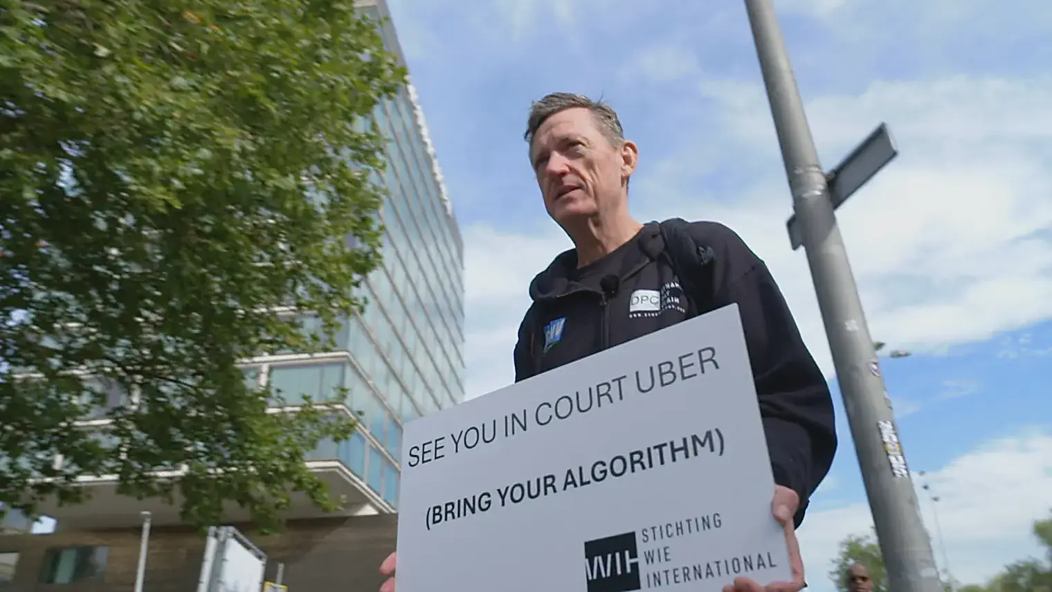Een actievoerder houdt een bord omhoog met de tekst See you in court Uber, bring your algorithm, met daaronder het logo van Stichting WIE International