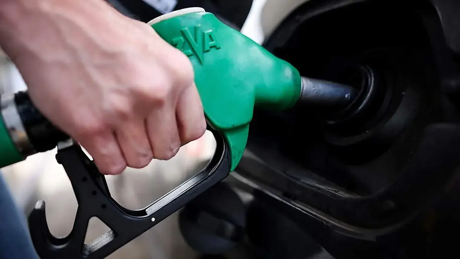 Close-up van een hand die een groen tankpistool in de vulopening van een auto houdt