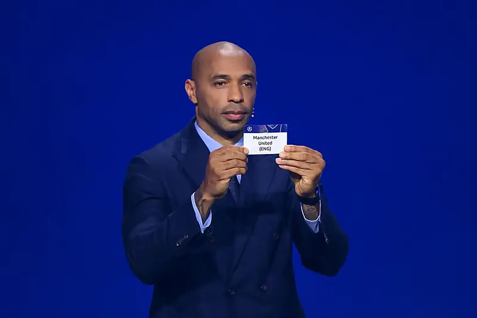Thierry Henry houdt bij de loting in Monaco een kaartje omhoog met daarop Manchester United