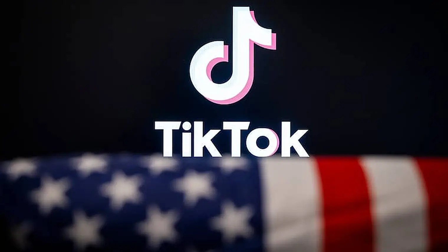 Het logo van TikTok op een donker scherm, met op de voorgrond de wazige sterren en strepen van de Amerikaanse vlag