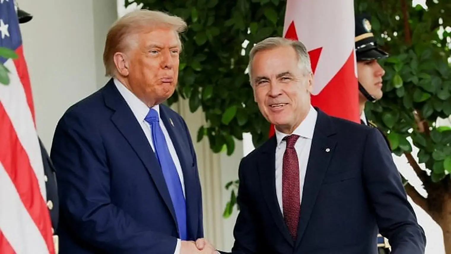 Donald Trump en Mark Carney geven elkaar de hand voor de Amerikaanse en de Canadese vlag bij het Witte Huis