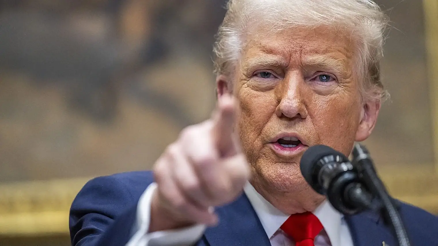 President Trump wijst met zijn vinger naar voren terwijl hij achter een microfoon spreekt