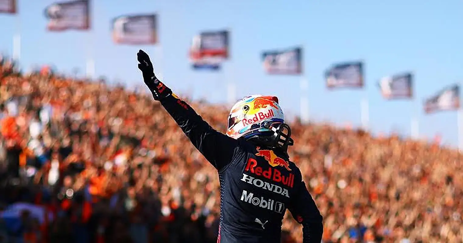Max Verstappen groet met opgestoken arm de oranje gekleurde tribunes op het circuit van Zandvoort