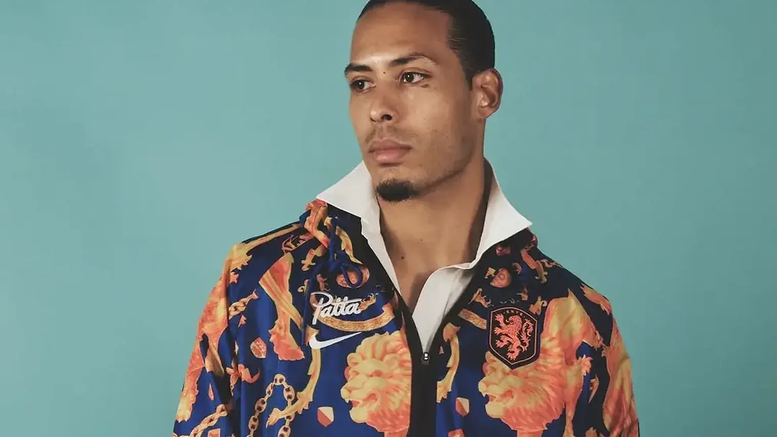 Virgil van Dijk in een blauw met oranje jack met leeuwenmotief, Patta-logo en Nike-swoosh, tegen een groenblauwe achtergrond
