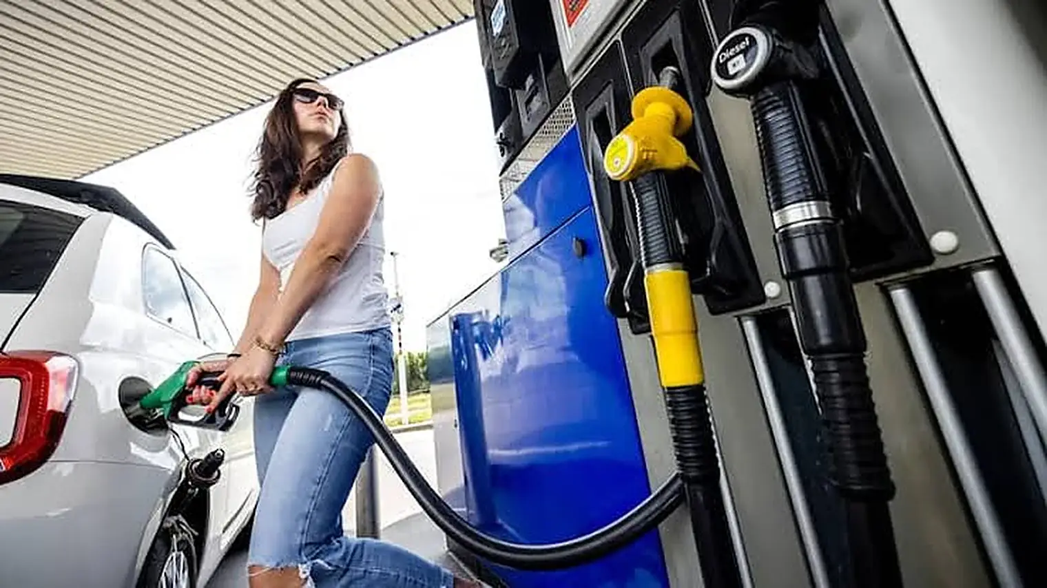 Een vrouw met een zonnebril tankt haar auto vol bij een blauwe pomp op een tankstation