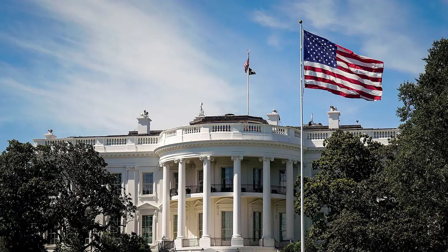 De zuidgevel van het Witte Huis met zuilen en balkon, met daarnaast een wapperende Amerikaanse vlag