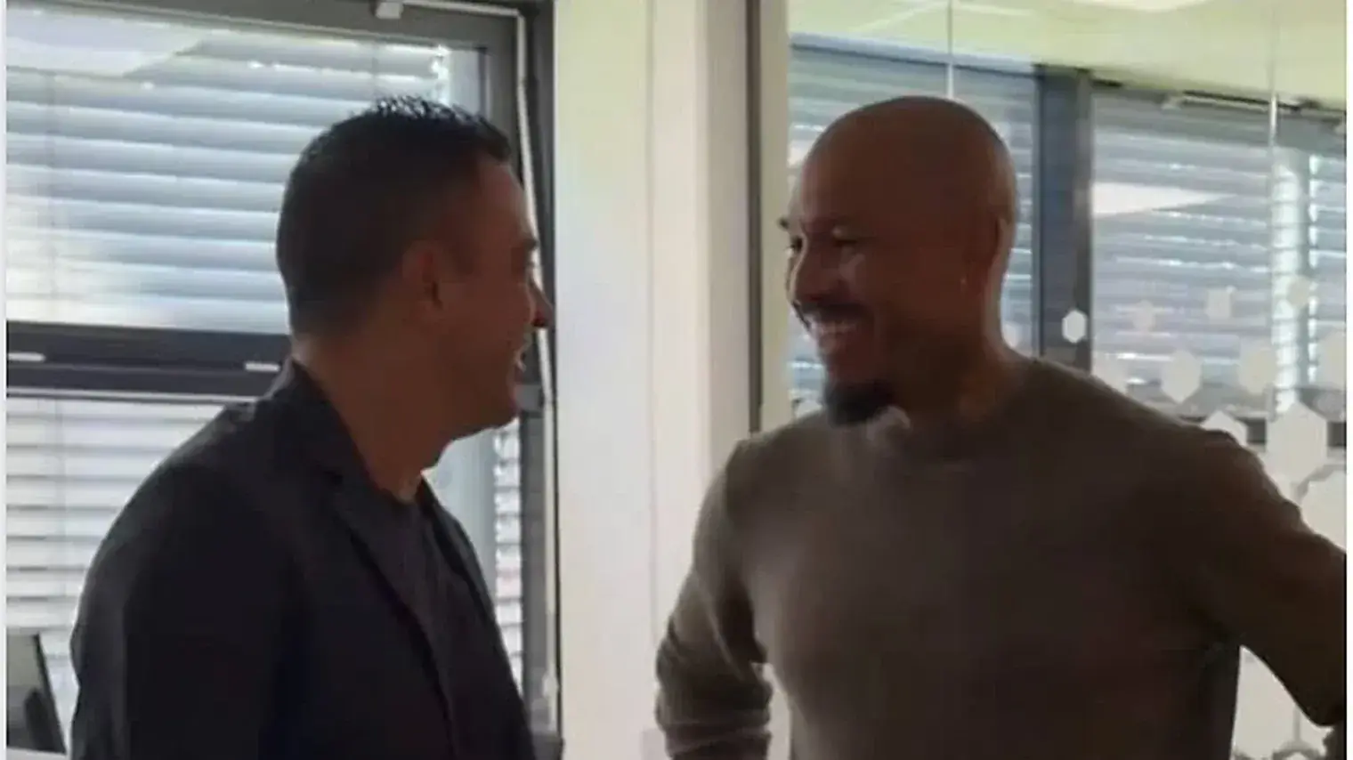 Xavi Hernandez in een zwart colbert lacht tegenover technisch directeur Nigel de Jong in een kantoor op de KNVB Campus