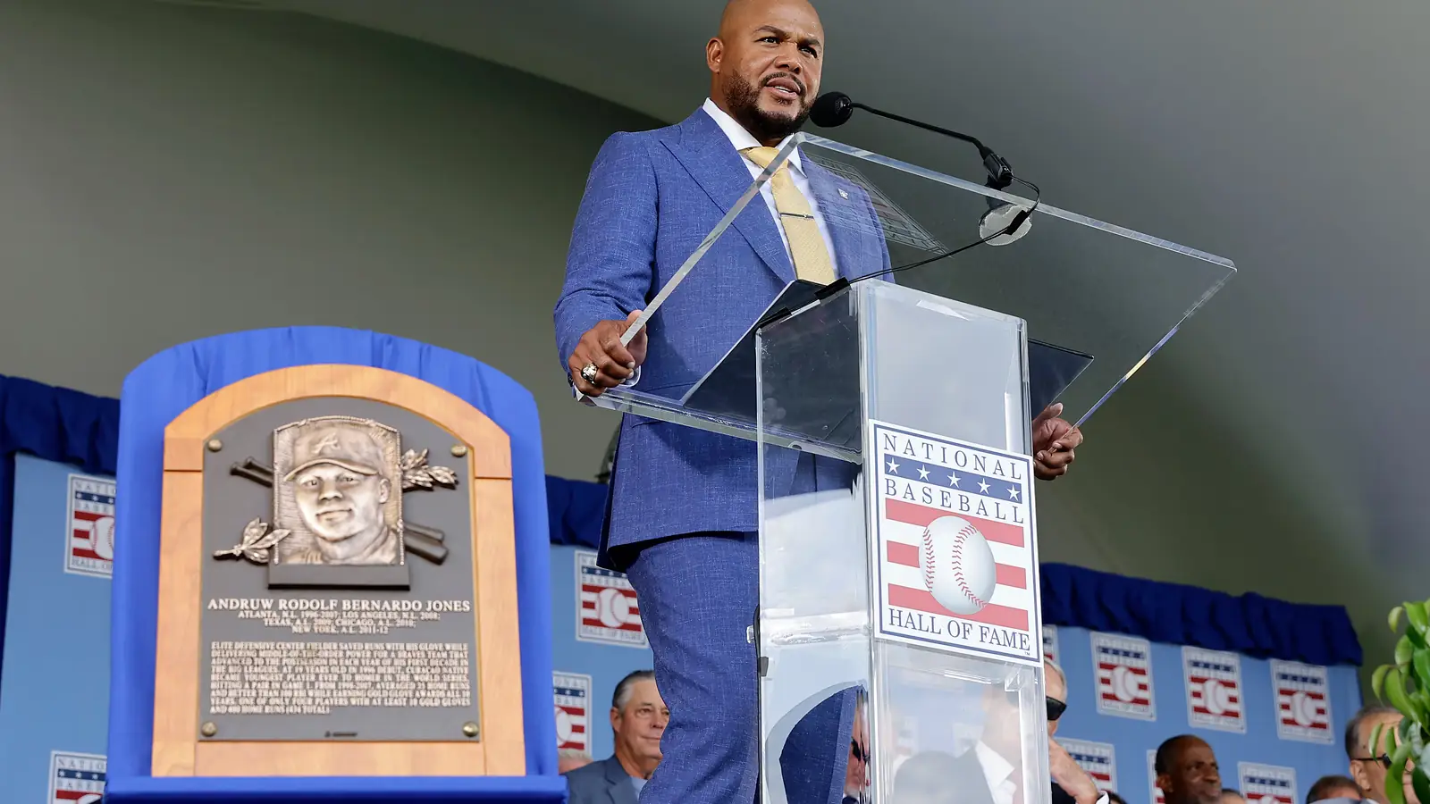 Andruw Jones spreekt in een blauw pak achter de lessenaar van de National Baseball Hall of Fame, naast zijn bronzen plaquette