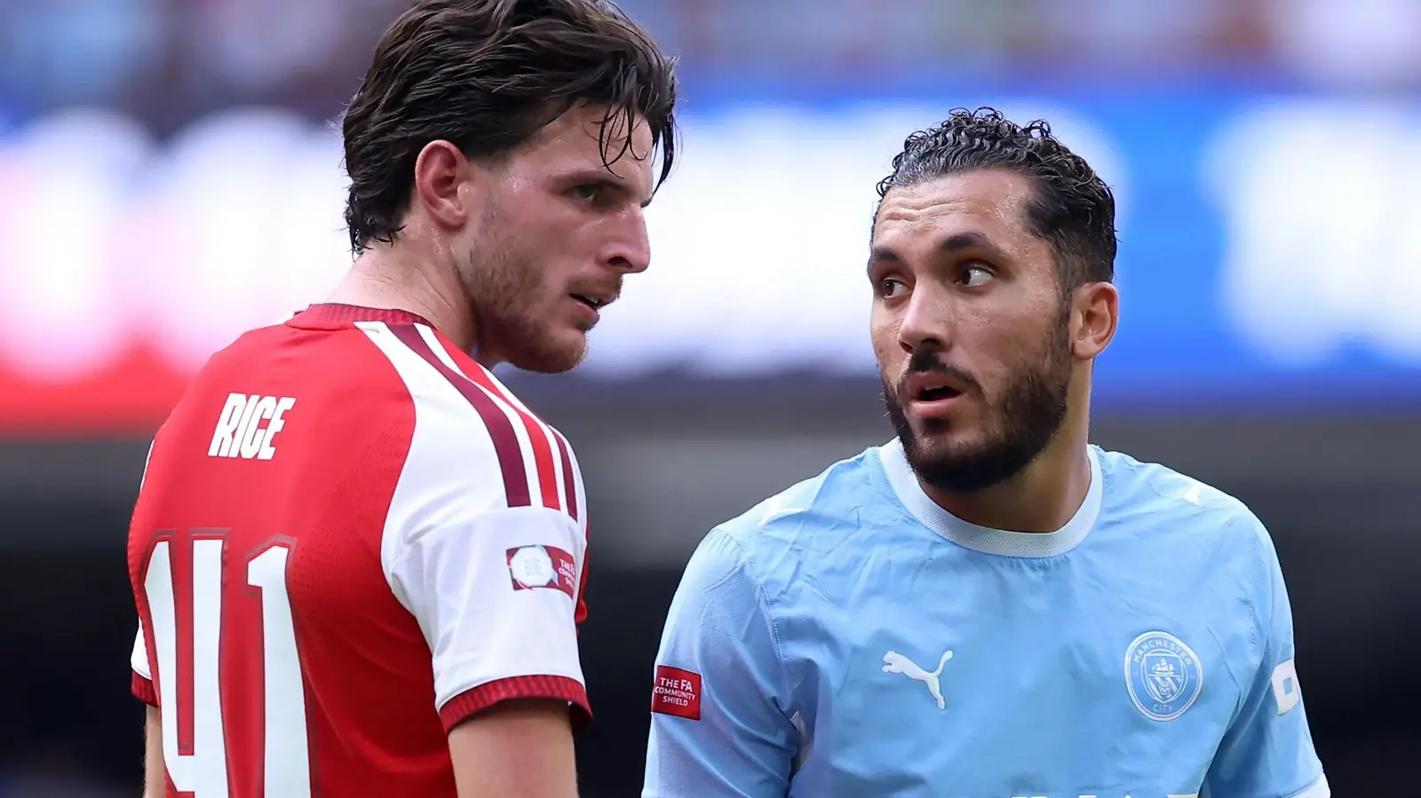 Declan Rice van Arsenal in het rood met witte shirt staat naast een speler van Manchester City in het lichtblauw, beiden met het embleem van de Community Shield op de mouw