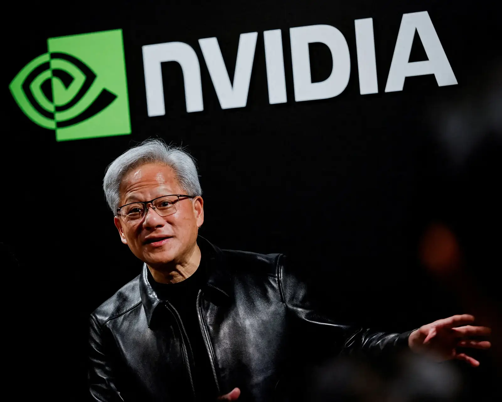 Jensen Huang van Nvidia in leren jack, pratend voor een groot Nvidia-logo op een donkere achtergrond