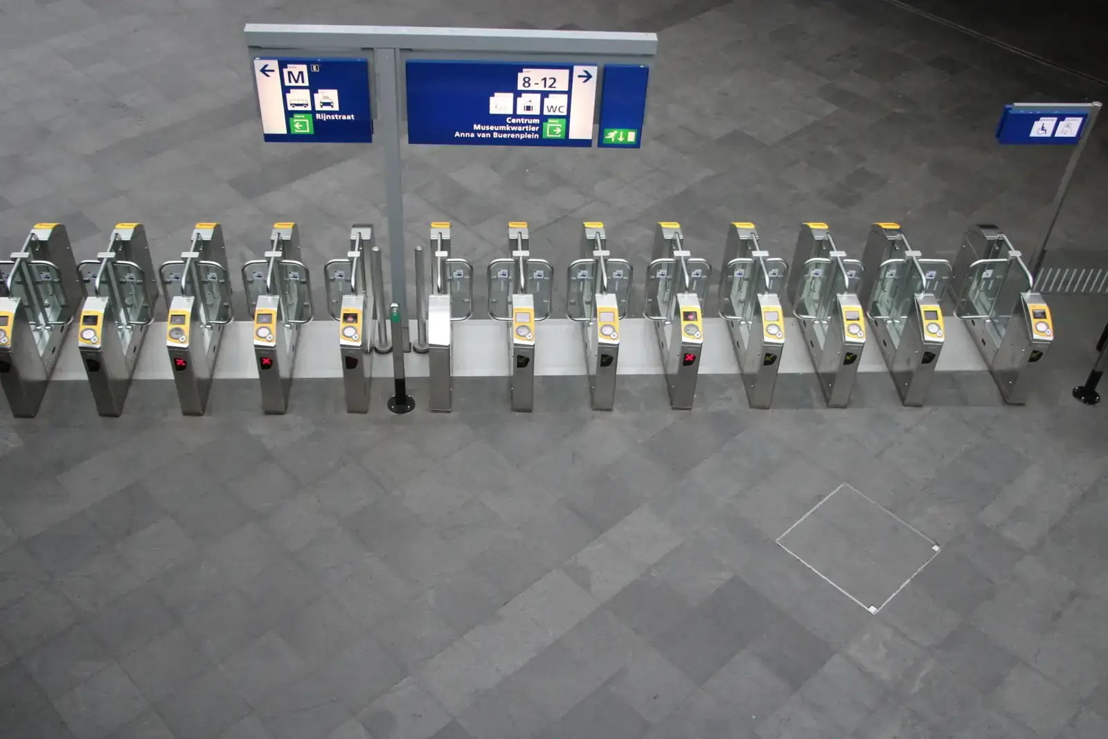 Rij gesloten toegangspoortjes met rode kruisjes in een verlaten stationshal, gezien van bovenaf
