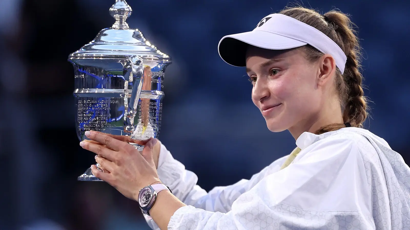 Elena Rybakina houdt de US Open-trofee omhoog en kijkt er glimlachend naar