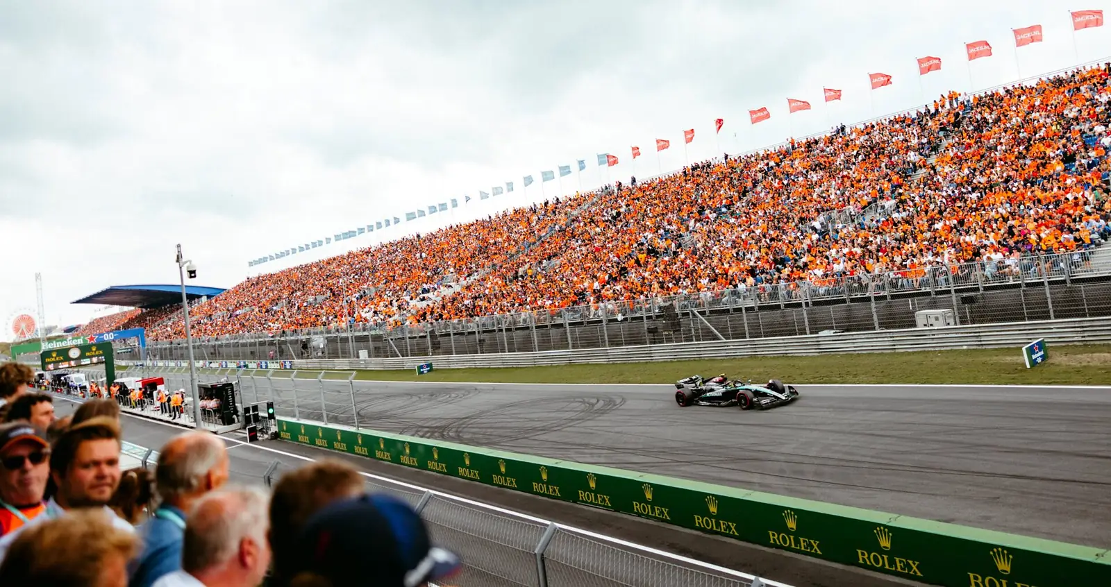 Volgepakte oranje tribune langs het rechte stuk van Zandvoort, met een Formule 1-auto op de baan