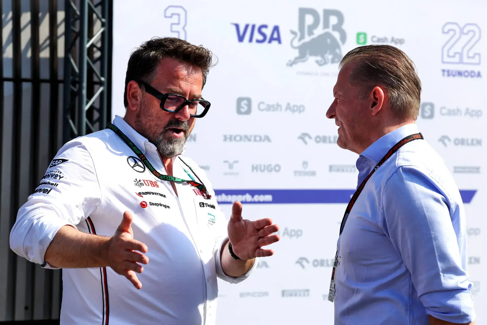 Gwen Lagrue in Mercedes-teamkleding in gesprek met Jos Verstappen in de paddock, voor de sponsorwand van Visa Cash App RB