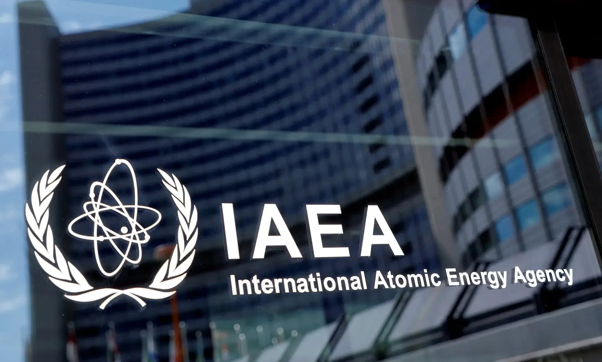Het logo van het Internationaal Atoomenergieagentschap op een glazen gevel, met het hoofdkantoor in Wenen weerspiegeld
