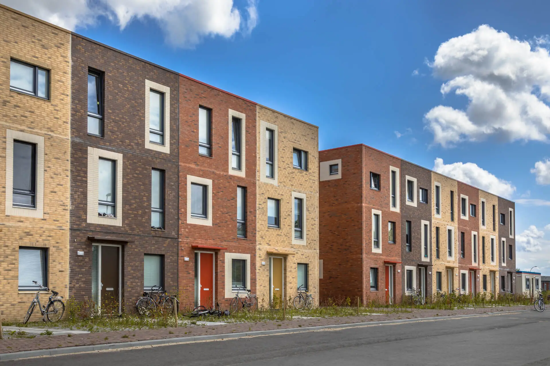 Straat met pas opgeleverde sociale huurwoningen van gele, bruine en rode baksteen, met fietsen tegen de voorgevels en jong groen langs de stoep