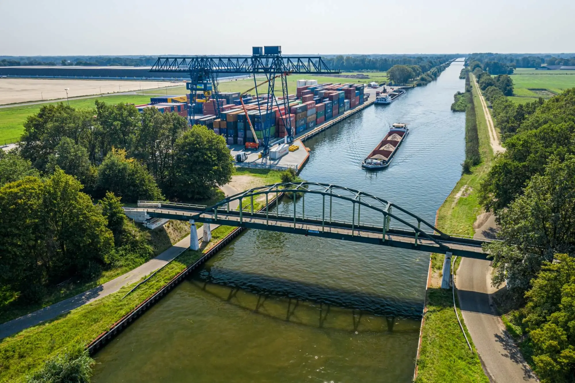 Luchtfoto van het Twentekanaal met containerterminal en een geladen vrachtschip onder een boogbrug