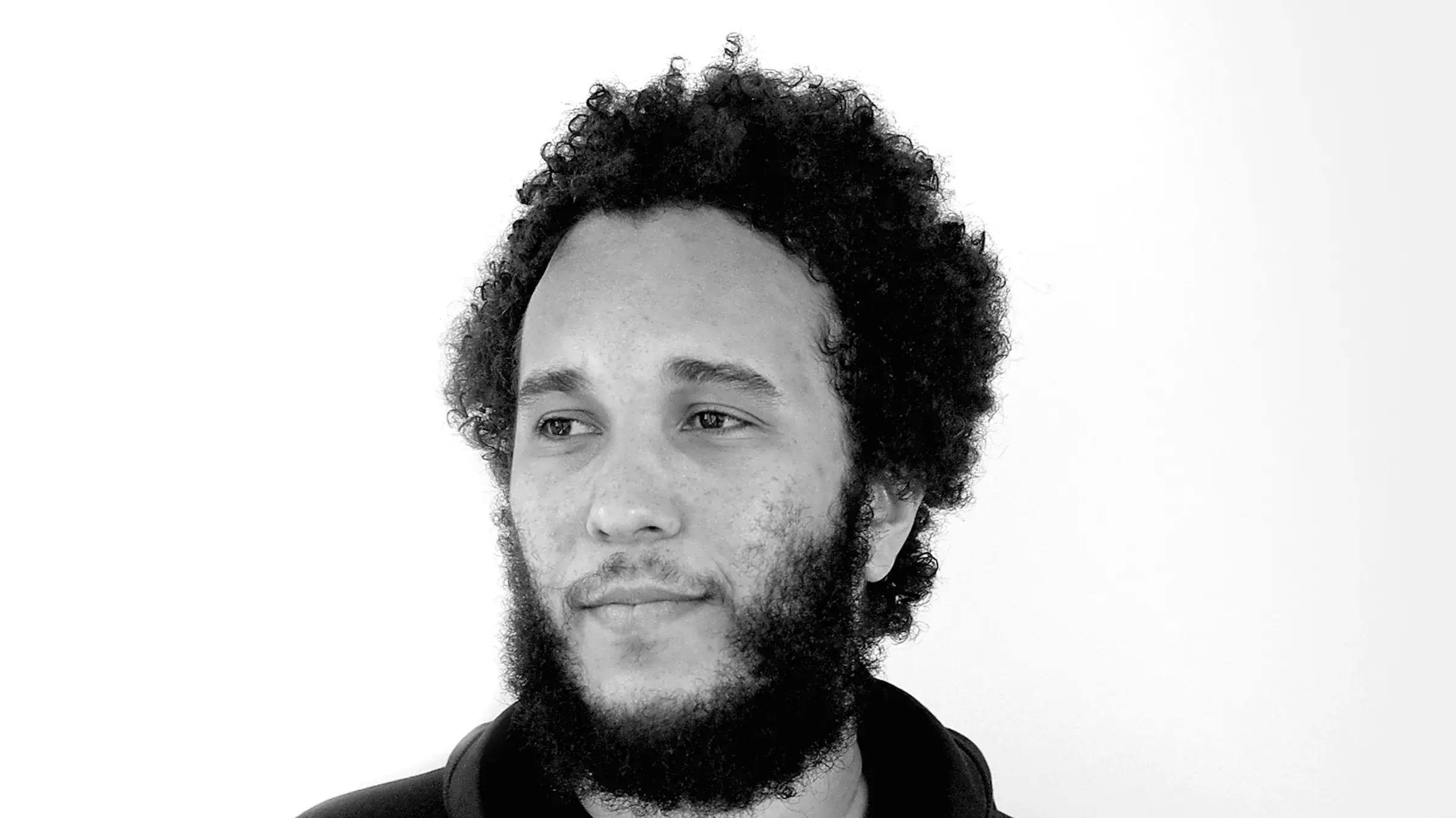 Zwart-witportret van dj Benny Rodrigues met krullend haar en baard, kijkend opzij tegen een witte achtergrond