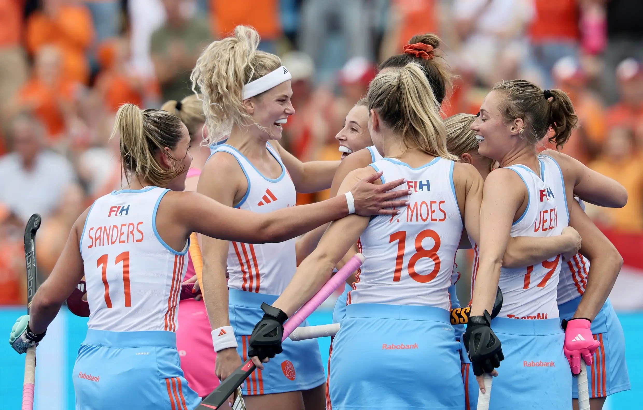 Nederlandse hockeysters vieren juichend een doelpunt in het witte uittenue, met een volle oranje tribune achter zich