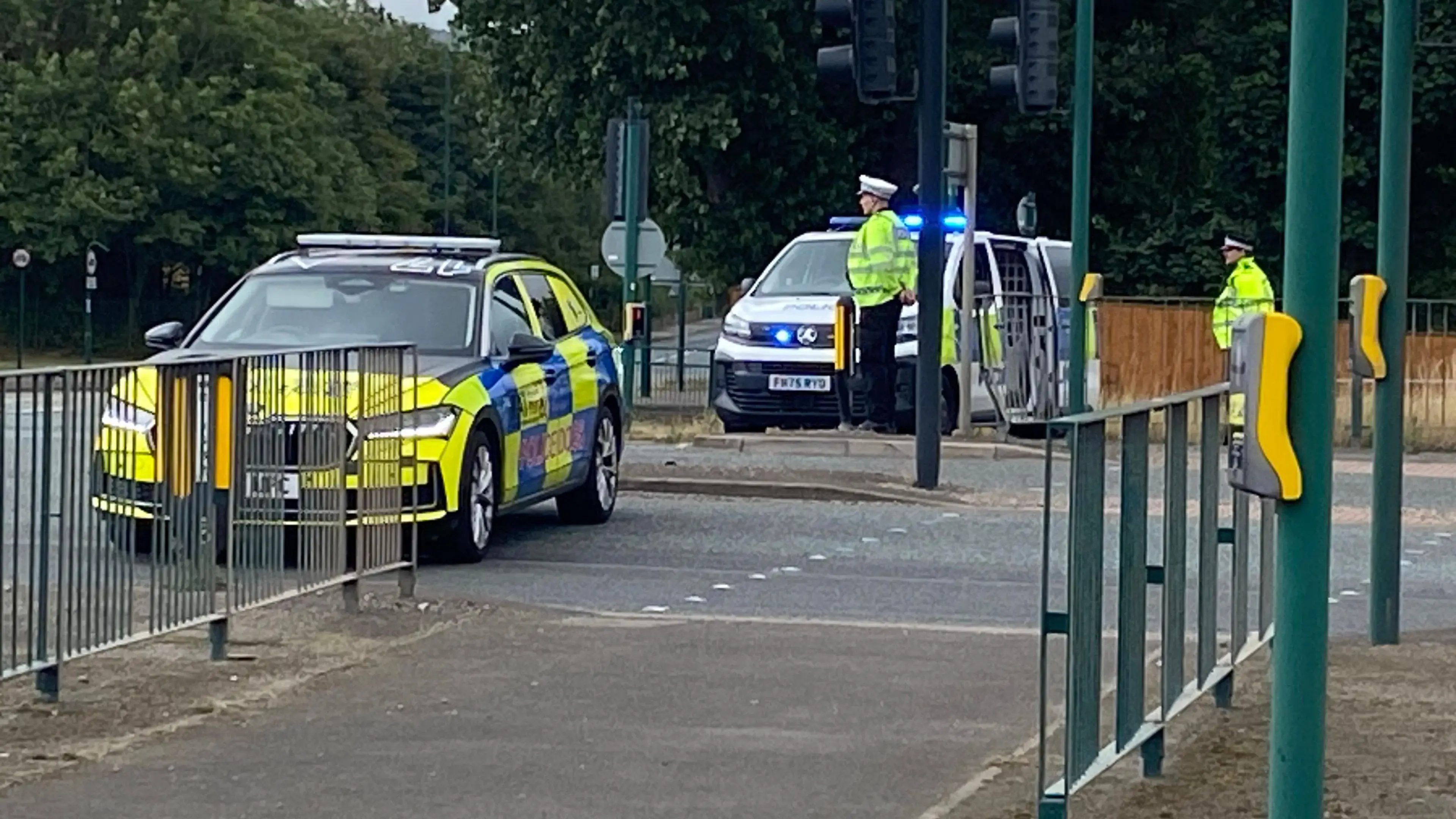 Politieauto dwars over de weg bij een kruispunt met verkeerslichten, met agenten in gele hesjes en een politiebus erachter