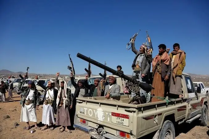 Houthi-strijders staan met geheven wapens op de laadbak van een pick-up truck in Jemen
