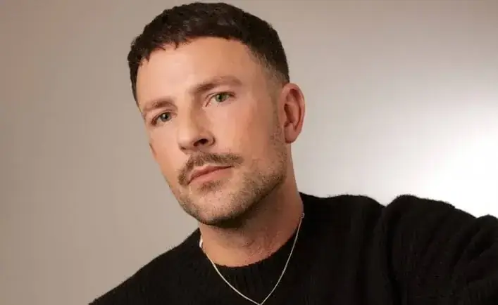 Portret van dj Shlømo in een zwarte trui tegen een lichte achtergrond