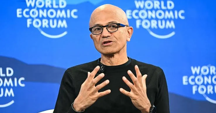 Mustafa Suleyman gebaart met beide handen tijdens een paneldiscussie, met een blauwe achtergrond van het World Economic Forum