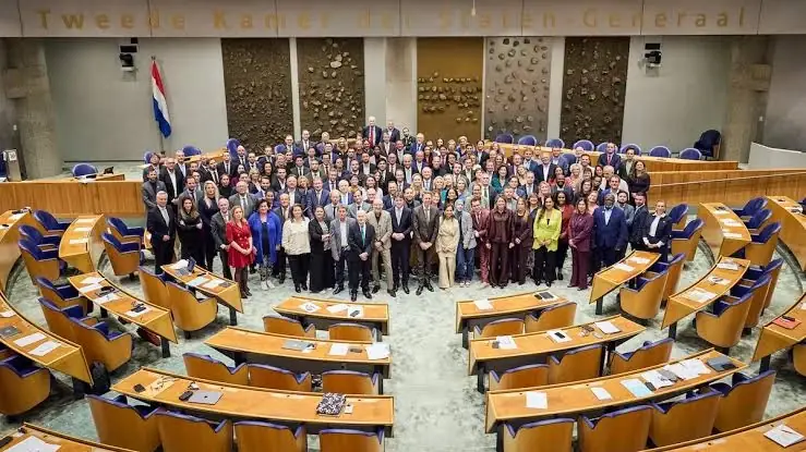 Groepsfoto van de Kamerleden in de plenaire zaal van de Tweede Kamer, onder de woorden Tweede Kamer der Staten-Generaal