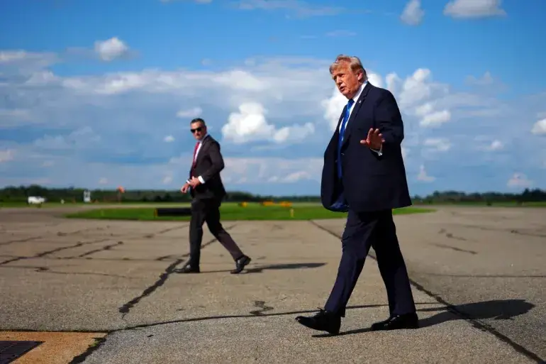 Donald Trump loopt met opgeheven hand over een leeg vliegveldplatform, met een beveiliger op de achtergrond