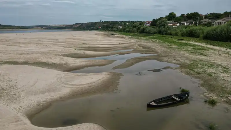 Brede zandbanken in een drooggevallen bocht van de Donau, met een houten roeiboot in een restje water langs de begroeide oever