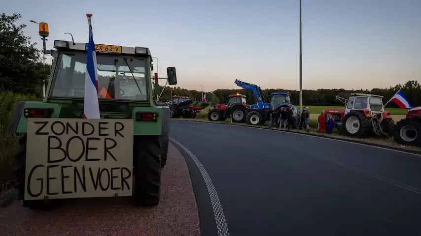 Tractoren langs een weg bij zonsopkomst met omgekeerde Nederlandse vlaggen en een bord met de tekst Zonder boer geen voer