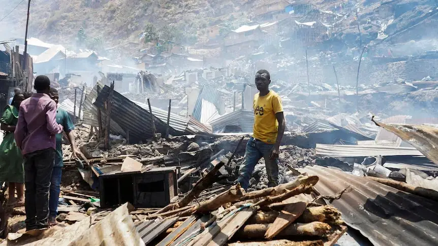 Inwoners van Bukavu staan tussen het verkoolde puin en de verwoeste golfplaten daken na de brand