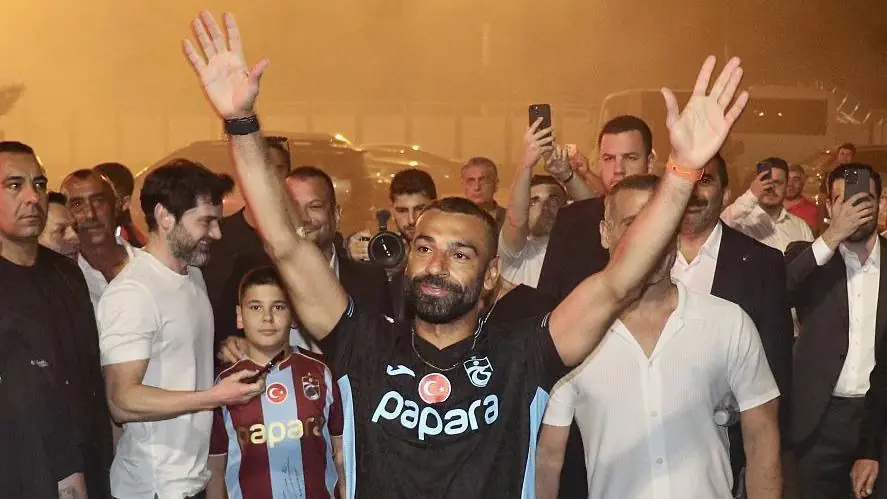 Mohamed Salah loopt met beide armen omhoog door een menigte in het donker, omringd door fans en beveiligers
