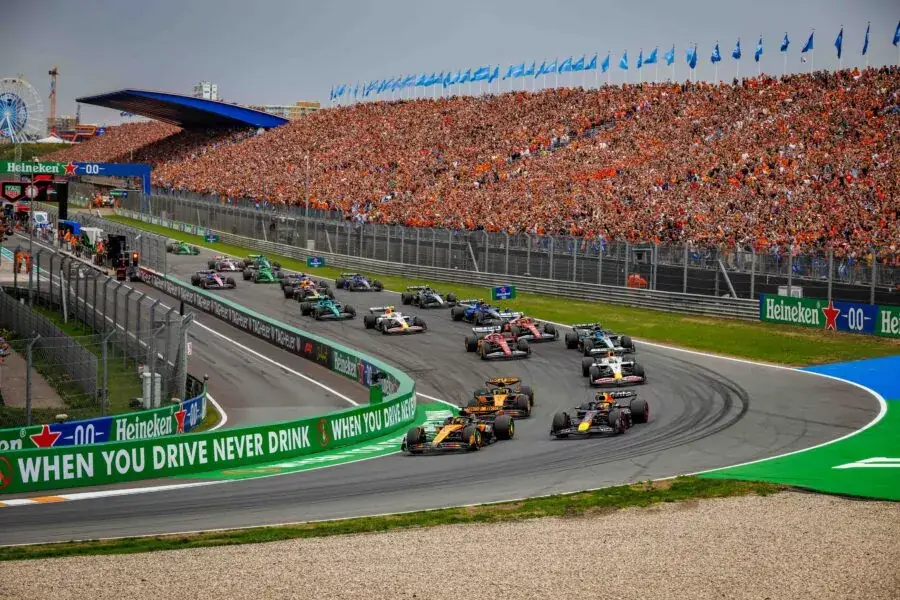 Het veld duikt na de start de eerste bocht van Zandvoort in, met daarachter een volgepakte tribune
