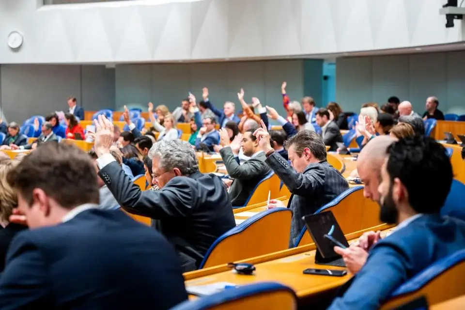 Kamerleden in de plenaire zaal steken hun hand op tijdens een stemming