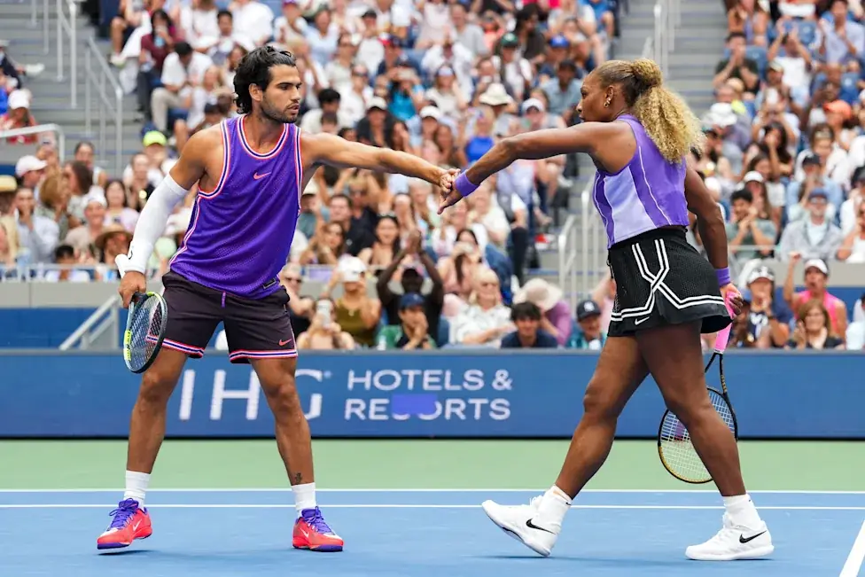 Carlos Alcaraz en Serena Williams geven elkaar een boks op de baan van het Arthur Ashe Stadium, met een volle tribune achter hen