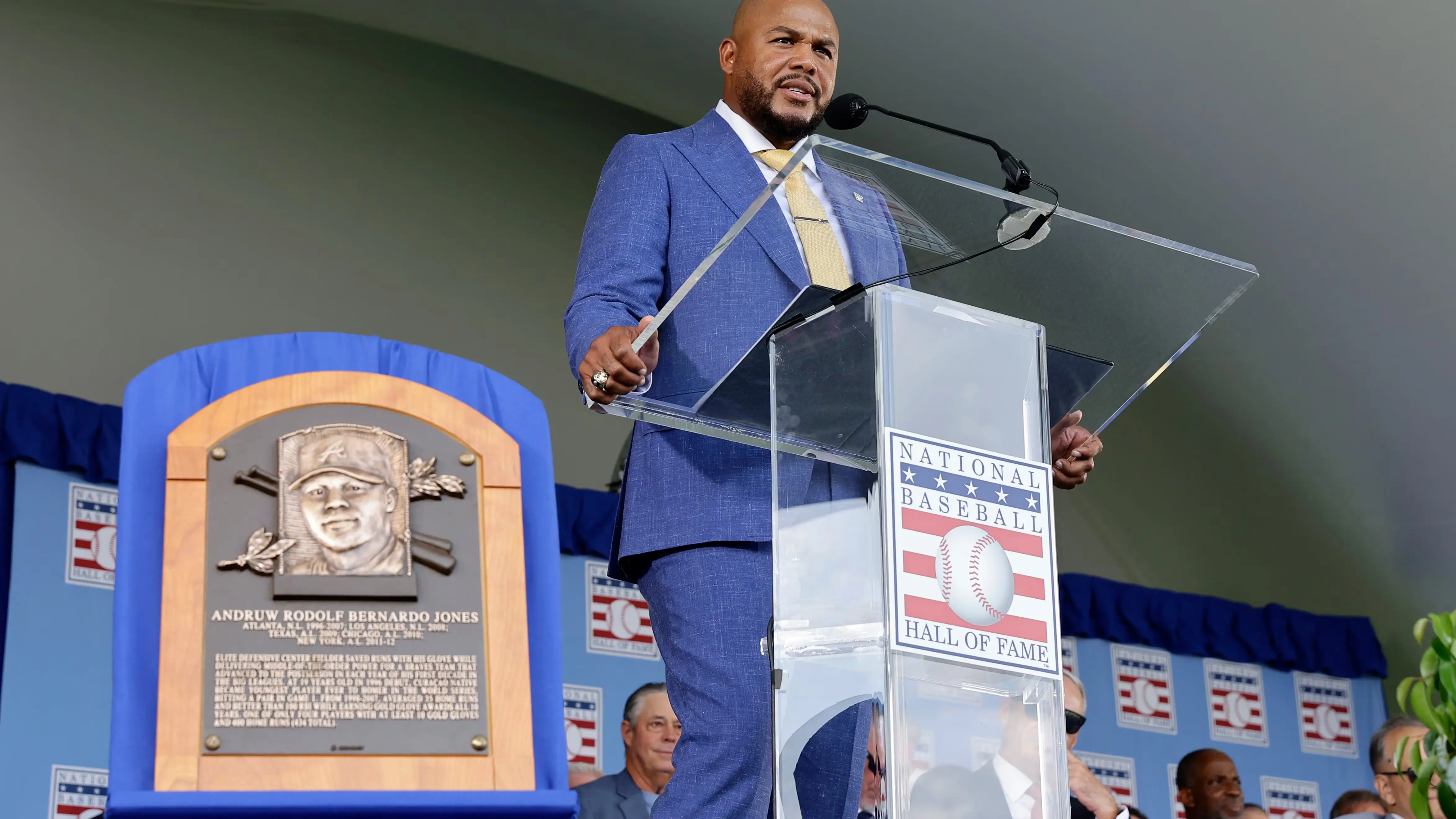 Andruw Jones spreekt in een blauw pak achter de lessenaar van de National Baseball Hall of Fame, naast zijn bronzen plaquette
