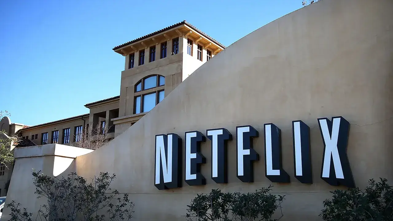 Het Netflix-logo in grote zwart-witte letters op een gebogen muur voor het kantoorgebouw van het bedrijf onder een blauwe lucht