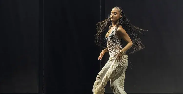 Tyla dansend op een donker podium, met lange gevlochten haren en een lichte broek met franjes